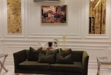 جدار مجلس فخم في فيلا بحي العقيق بالرياض مزين ببراويز وفوم (بانوهات) نيو كلاسيك بلون أوف وايت ناعم مدمج مع إضاءة أبليكات جدارية ذهبية كلاسيكية